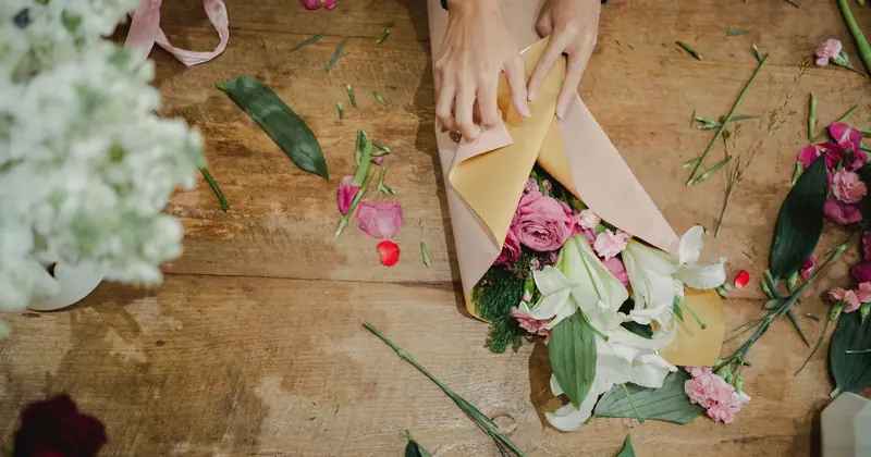 From above of crop faceless female florist holding bouquet of fresh flowers and creating bouquet