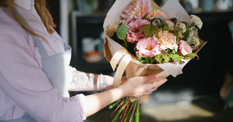 Close-up of a florist holding a colorful bouquet of flowers indoors, showcasing floral elegance.