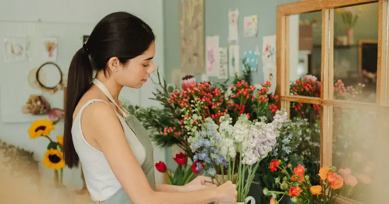 Side view of serious female florist arranging fresh flowers in vase while working in florist studio