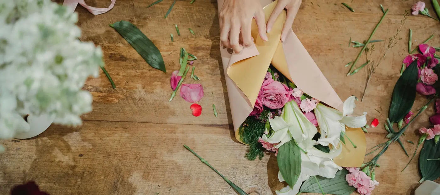 From above of crop faceless female florist holding bouquet of fresh flowers and creating bouquet